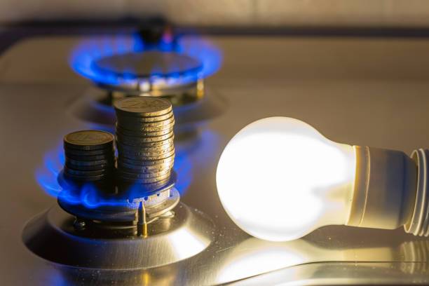 Light bulb on next to lit gas cooker, with coins next to it. Energy and gas costs